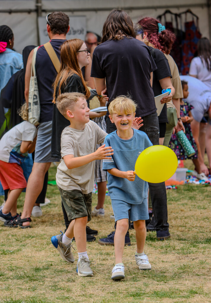 Children playing with balloons at community event, fair, or festival full of activities.