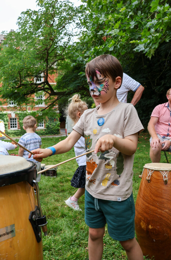 Young boy with painted face playing the drums at the Sticks N Stones Festival in Medway Kent